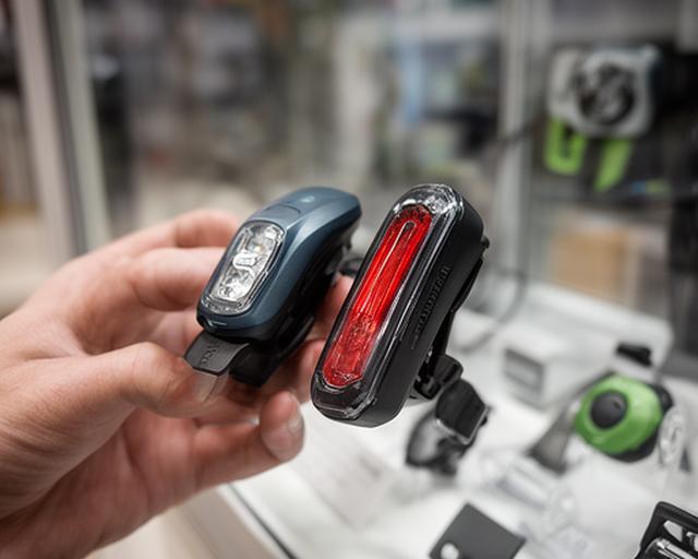 Mão a comparar duas luzes traseiras de bicicleta numa vitrina de loja